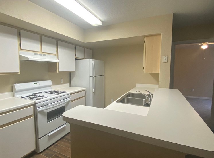 Kitchen featuring white cabinets, white appliances, white countertop, gas stove, and fluorescent tube lighting
